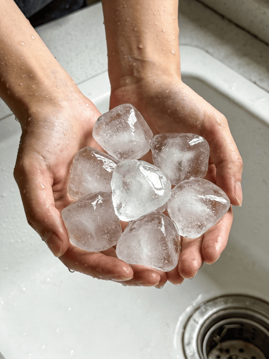 jimeng-2026-03-09-4777-双手捧着7颗又大又透的不规则形状的冰块，背景白色厨房水槽，手被冰水打湿.png